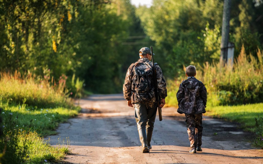 father and son walking through the woods to go deer hunting. if they find a deer to shoot, they will bring it home and make deer jerky