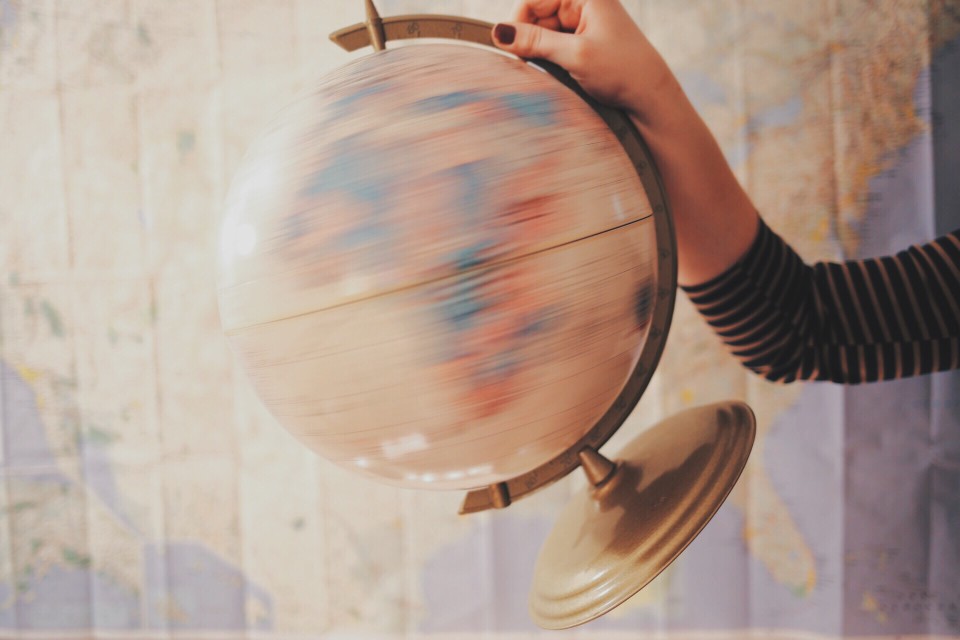 arm in photo frame holding a spinning globe in front of a map