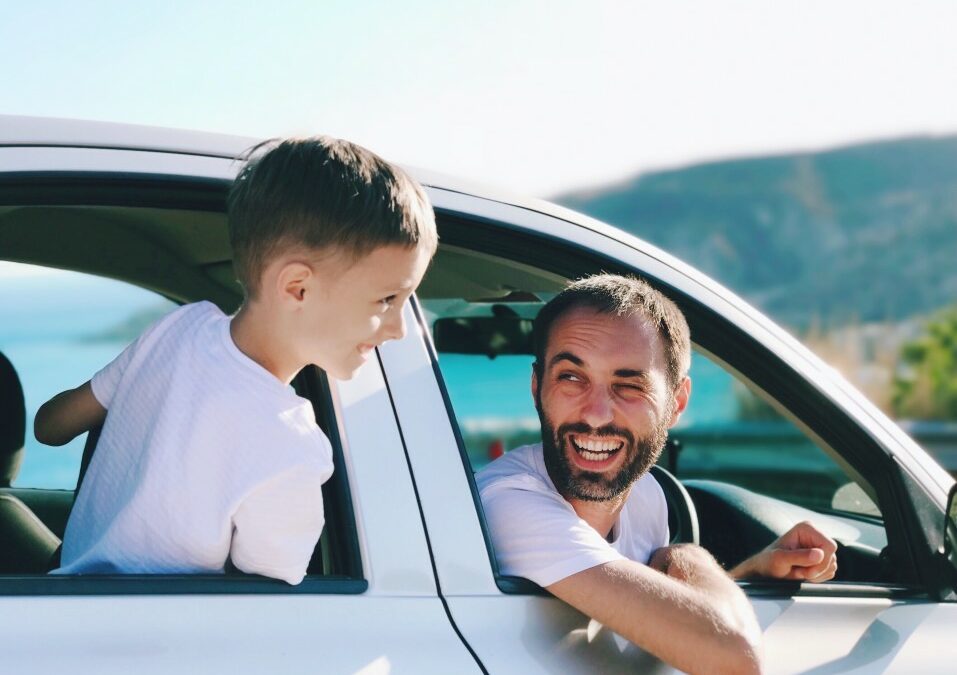 father and son duo looking at each other out of car windows during a road trip